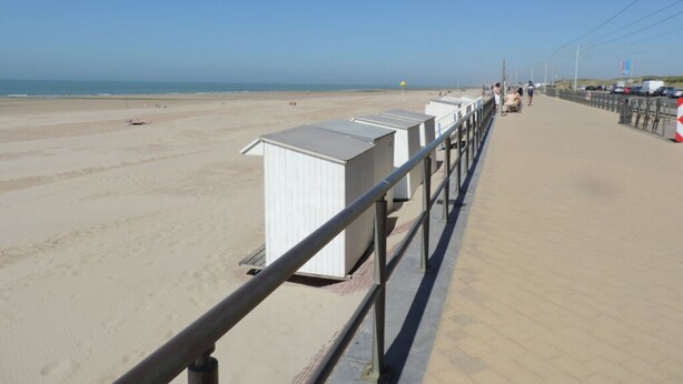 Ein Promenadweg am Strand mit weißen Strandhütten und einem Metallgeländer.