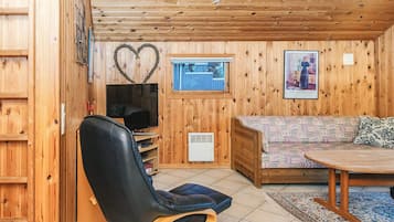 Un acogedor interior de cabaña con techo de madera, televisor, sofá y mesa de comedor.