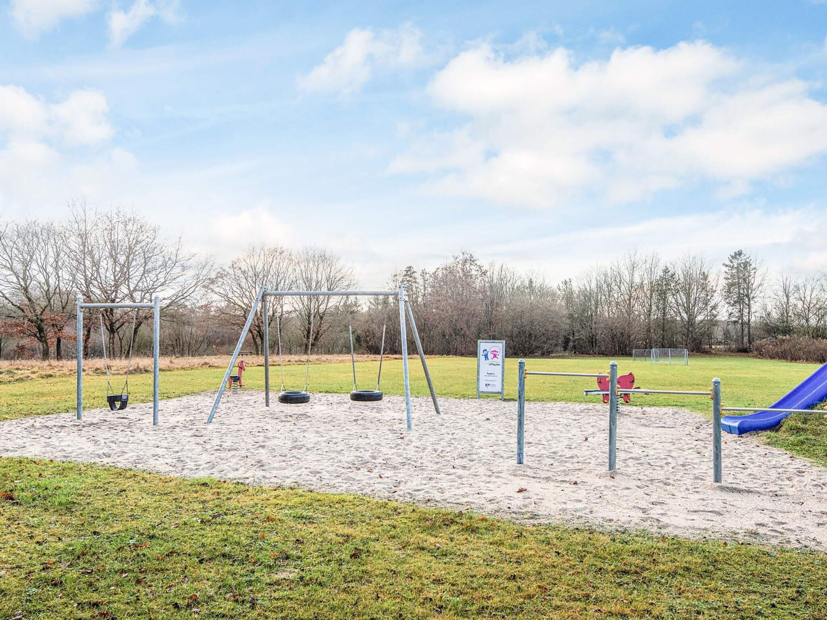 Un parque infantil con tobogán, columpios y neumáticos colgantes.