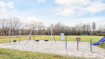 Un parque infantil con tobogán, columpios y neumáticos colgantes.