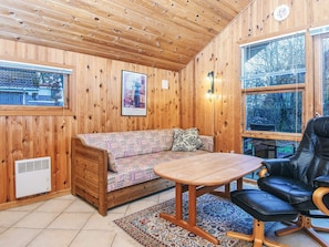A cozy cabin interior with a wooden ceiling, a sofa, a table, and a leather chair. - 4 Person Holiday Home in Hovborg (Hovborg)