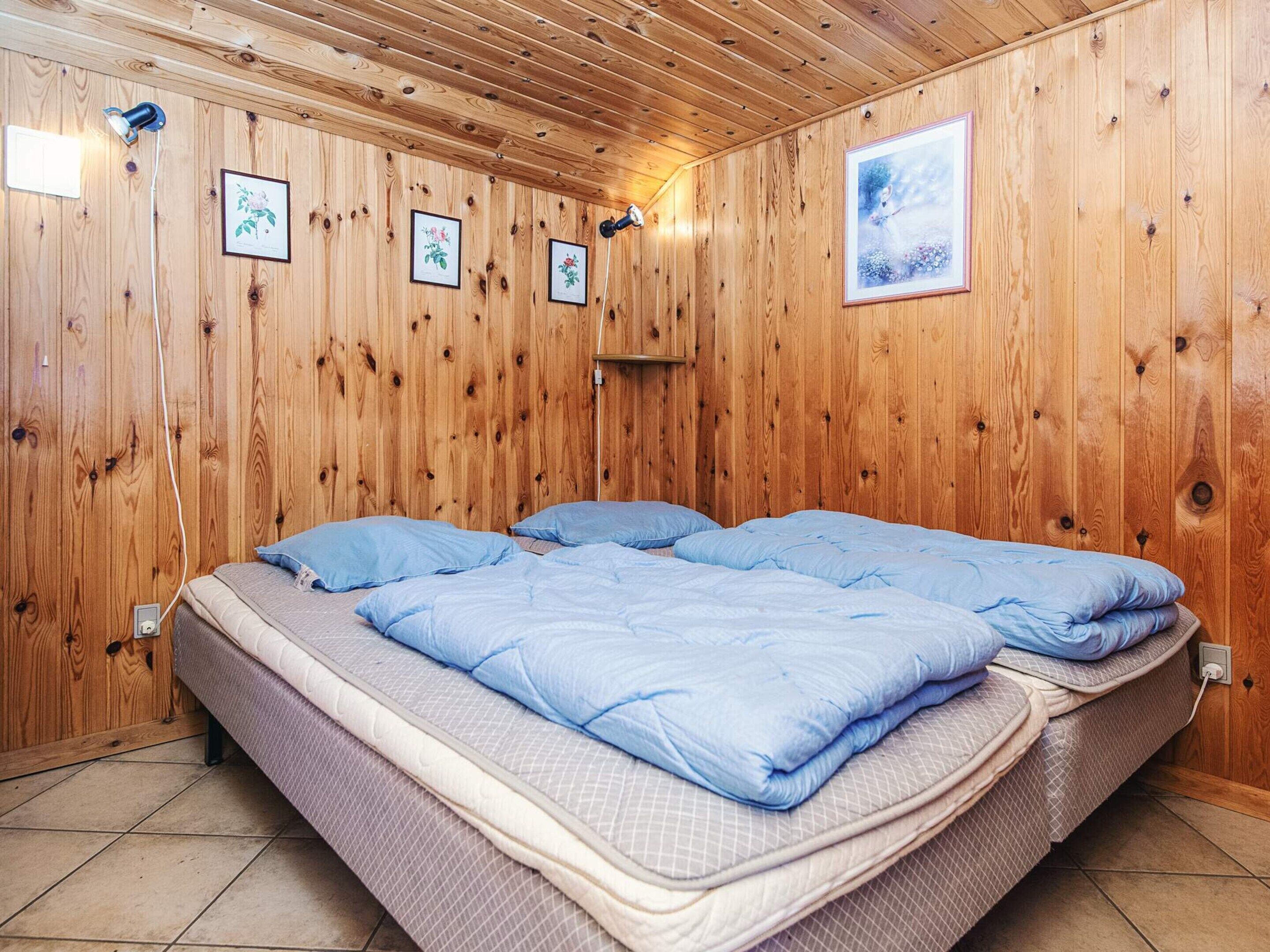 A wooden-paneled room with a bed, framed pictures, and a wall socket.