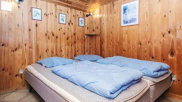 A wooden-paneled room with a bed, framed pictures, and a wall socket.
