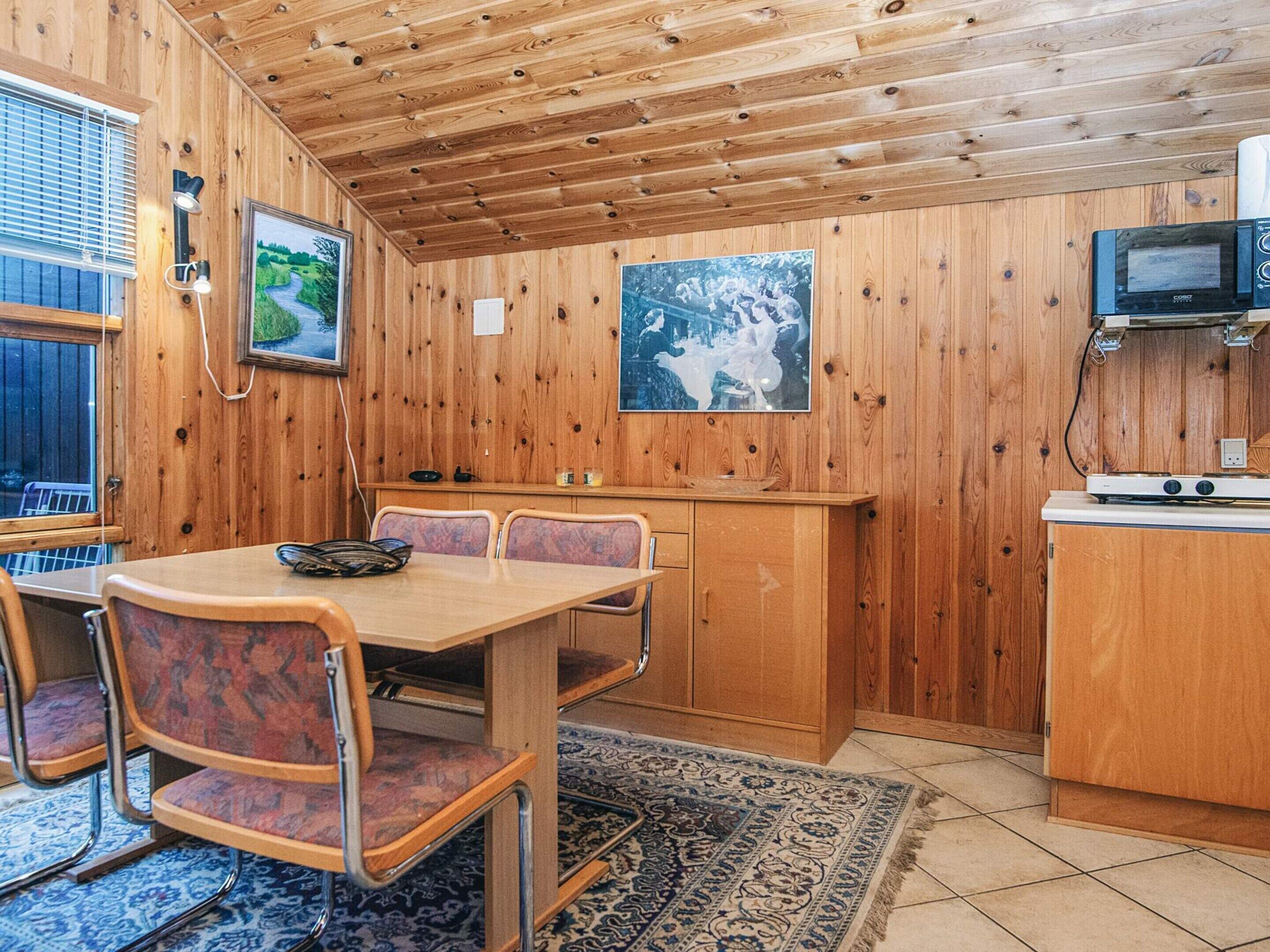 A wooden interior with a dining table, chairs, a kitchen area with a microwave, and a rug.