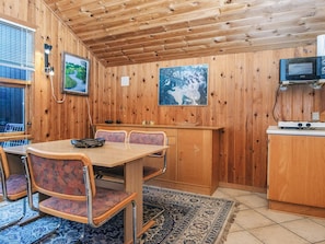 A wooden interior with a dining table, chairs, a kitchen area with a microwave, and a rug. - 4 Person Holiday Home in Hovborg (Hovborg)