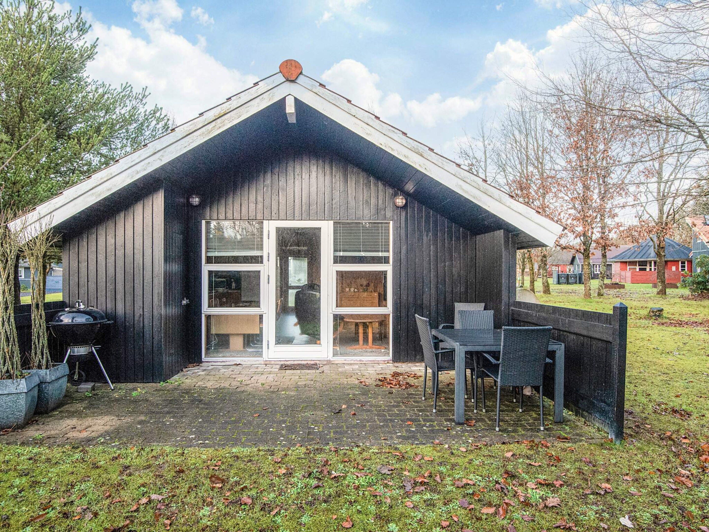 A wooden cabin with a large sliding glass door, a patio with outdoor furniture, and a barbecue grill.