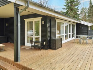 A black cabin with a wooden deck, a covered patio, and a table with chairs.