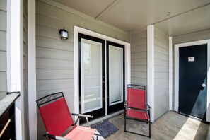 A covered porch with two red chairs, a black door, and a light fixture. - I043 - Cozy 2BD | Pool | DFW South 183/161 (Irving)