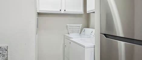 A compact laundry room with a front-loading washer and dryer, a stainless steel refrigerator, and white cabinetry above the appliances.