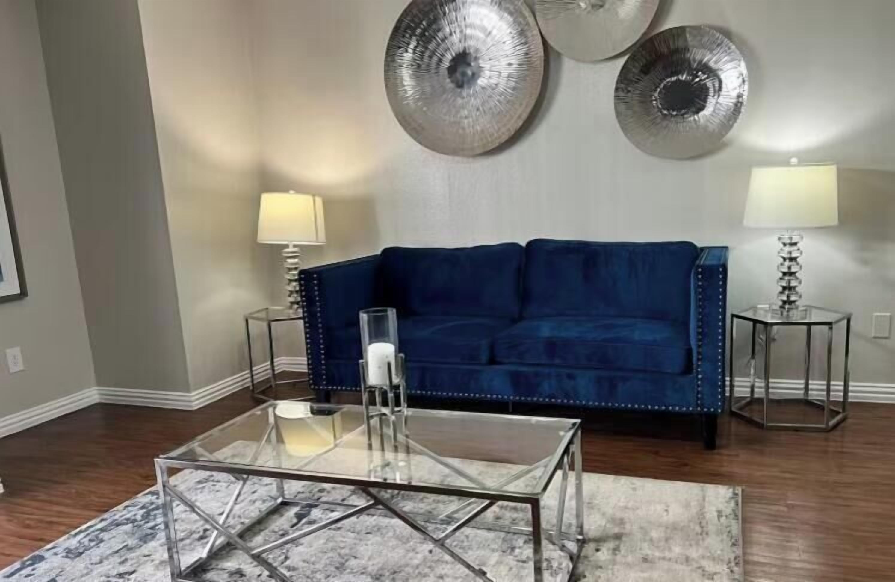 Un salon avec un canapé bleu, deux tables d’appoint avec des lampes, une table basse en verre et des miroirs décoratifs sur les murs.