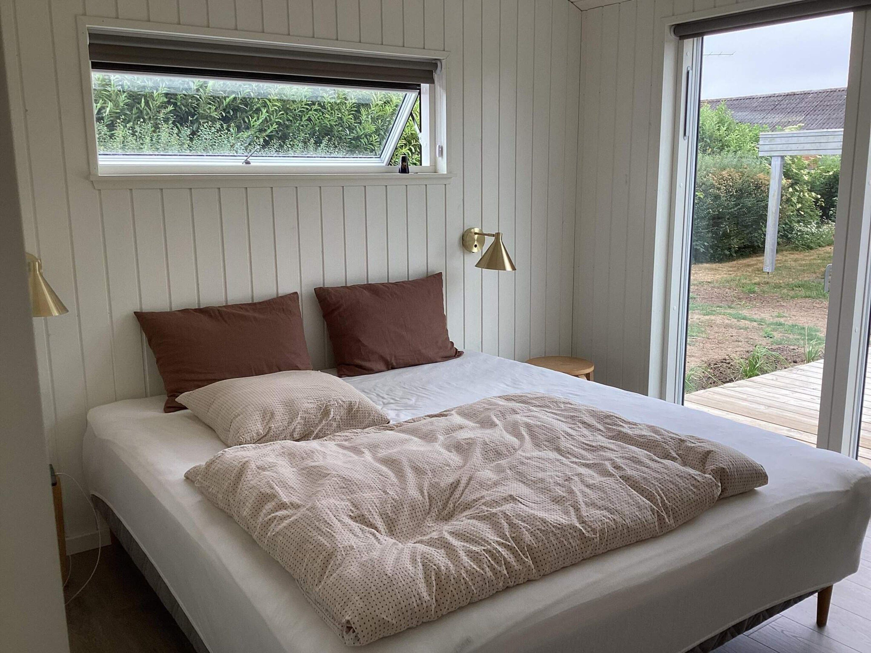 A bed with a window above it, a bedside lamp, and a view of a garden.