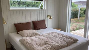 A bed with a window above it, a bedside lamp, and a view of a garden.