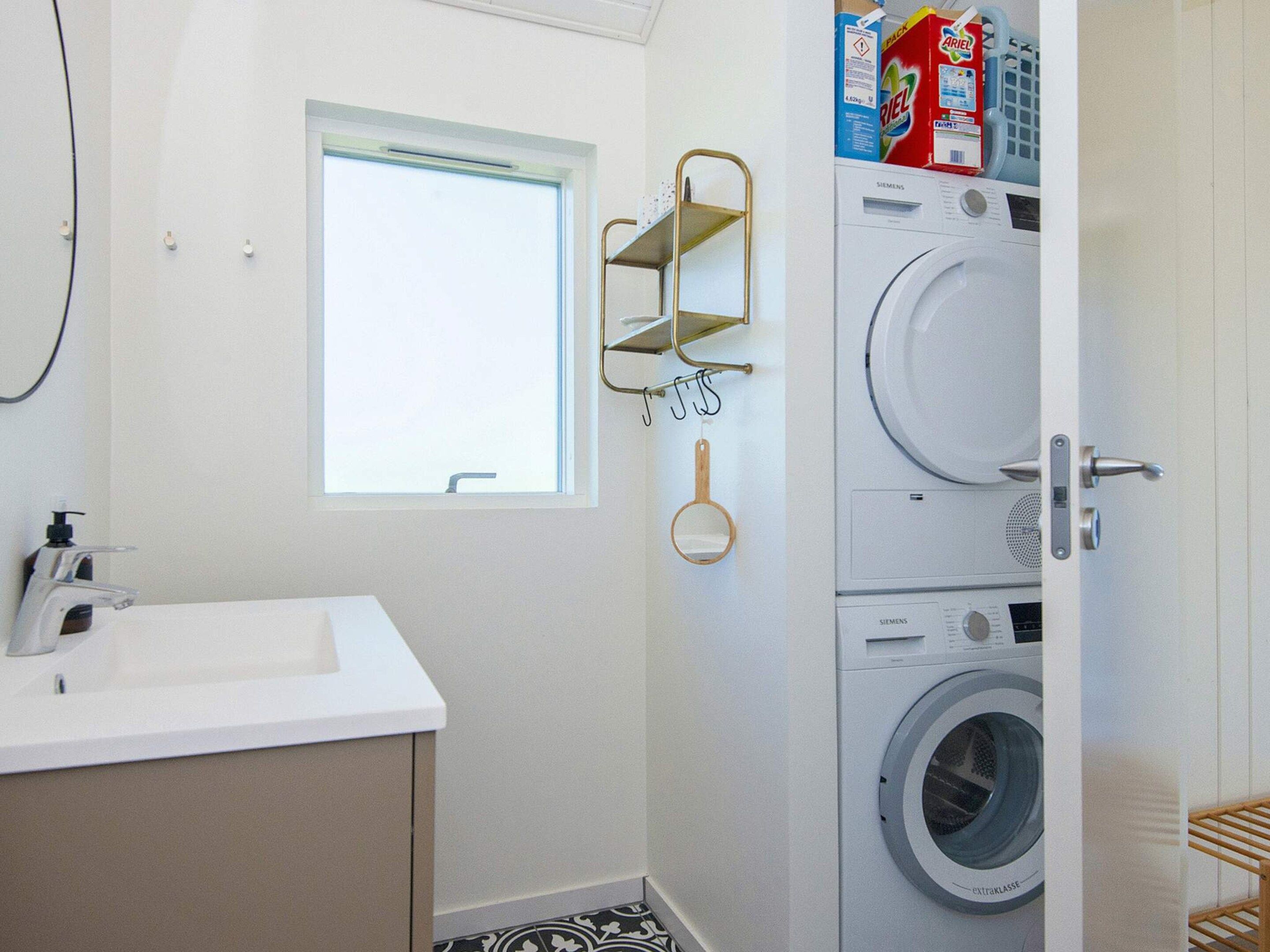 A compact bathroom with a sink, a window, a washing machine, and a shelf with hanging items.