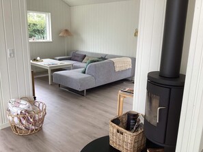 A cozy room with a grey sofa, a small table, a wicker basket, and a black wood-burning stove. - 4 Star Holiday Home in Juelsminde (Juelsminde)