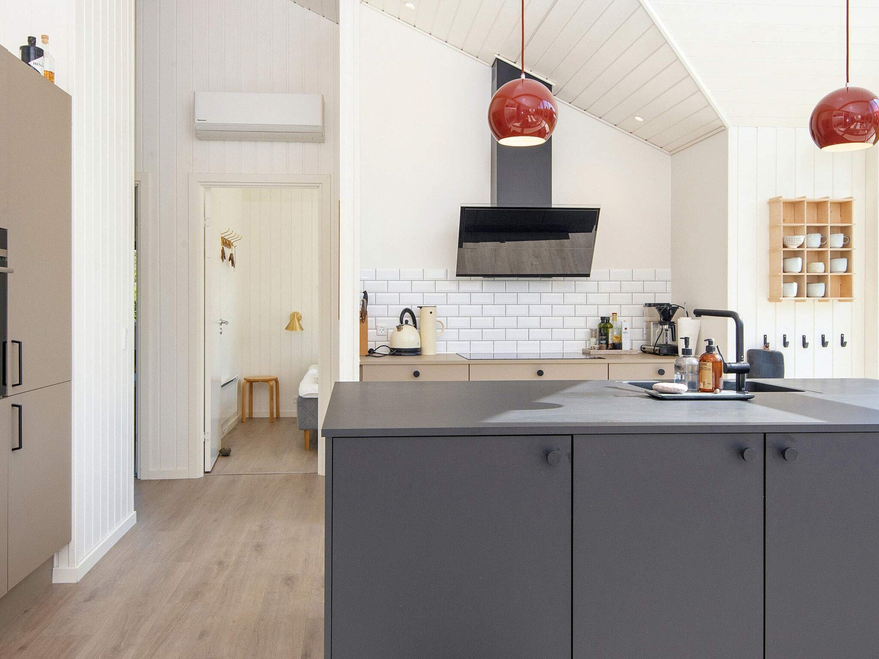 Une cuisine moderne dotée d’un îlot central, de luminaires suspendus et d’un dosseret de carrelage blanc.