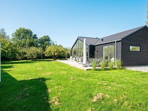 A modern house with a large glass window, a wooden deck, and a grassy yard. - 4 Star Holiday Home in Juelsminde (Juelsminde)