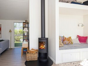 A cozy living room with a black wood-burning stove, a bookshelf, a wicker basket, and a comfortable seating area with pillows. - 4 Star Holiday Home in Juelsminde (Juelsminde)
