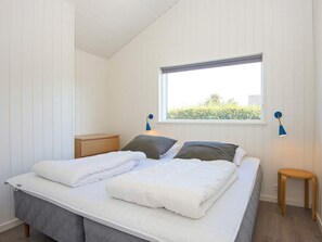 Ett sovrum med en säng, sängbord, ett fönster och utsikt över grönområden utanför.
