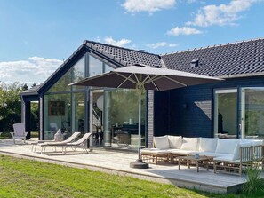 A modern house with a glass-enclosed patio, outdoor furniture, and a clear sky. - 4 Star Holiday Home in Juelsminde (Juelsminde)