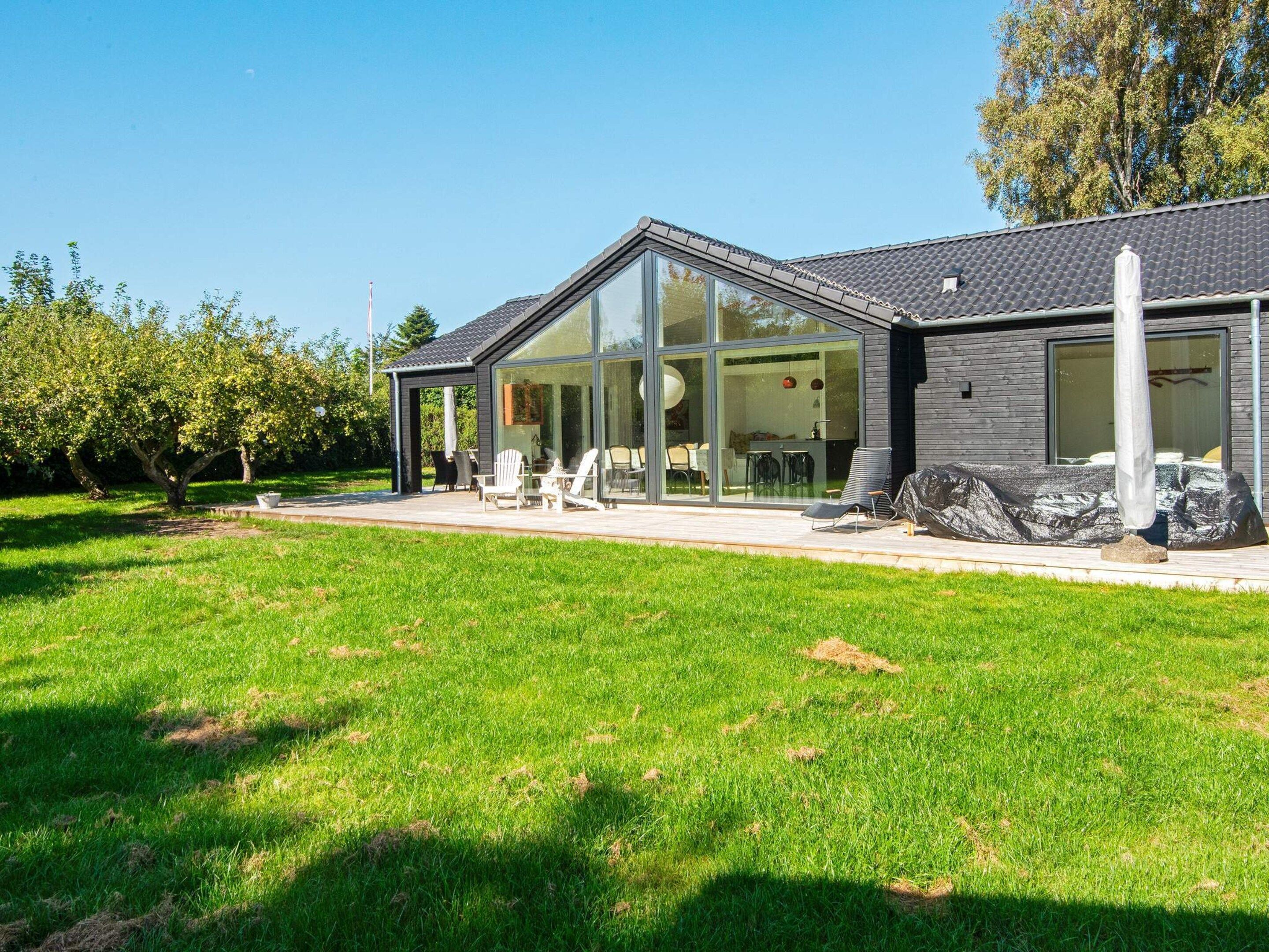 Una casa moderna con un amplio ventanal, un patio con mobiliario exterior y un césped bien cuidado.