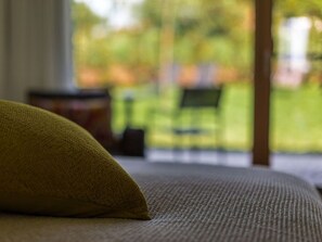 Nahaufnahme einer strukturierten Stoffoberfläche, vermutlich Teil eines Bettes oder Sofas, mit unscharfem Blick auf eine Außenanlage durch ein Fenster.