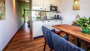 Eine moderne Küche mit weißen Schränken, einer Mikrowelle und einer Kaffeemaschine. Ein Holztisch mit Stühlen und eine Blumenvase ergänzen das Bild.