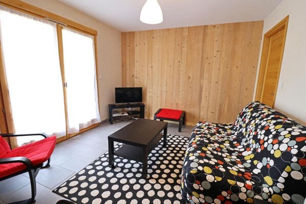A living room with a sofa, a coffee table, a TV on a stand, and a red chair.