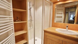 Un baño con ducha de vidrio, tocador de madera con lavamanos y espejo sobre el tocador.