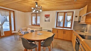 Una habitación acogedora con techo de madera, una mesa de comedor con sillas, un sofá y una zona de cocina con armarios y estufa.