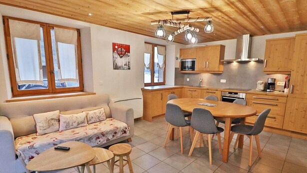Una sala de estar acogedora con un sofá, una mesa de comedor con sillas y una zona de cocina con armarios de madera y una estufa.