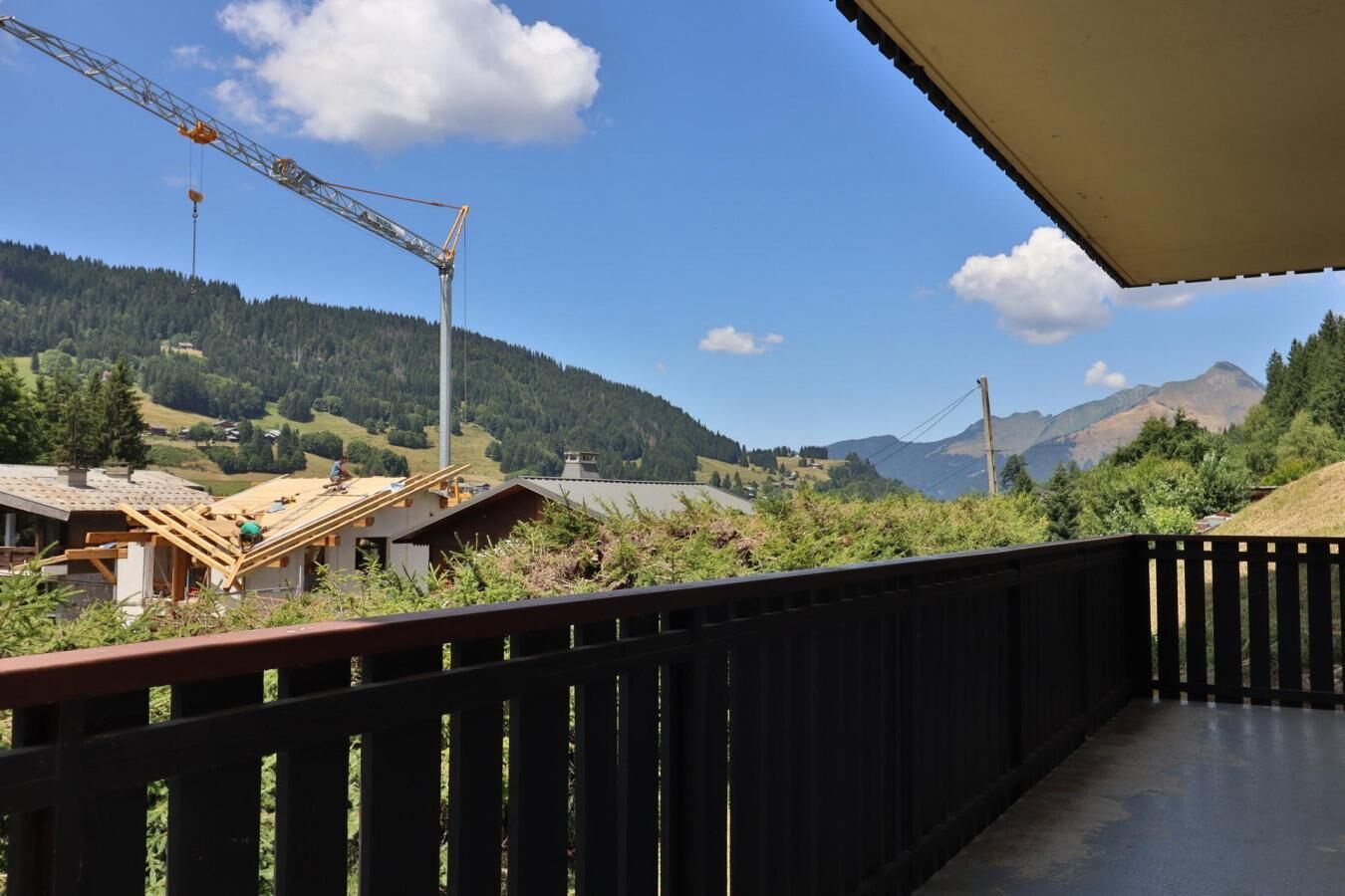 A construction site with a crane and a partially built structure, surrounded by a forested landscape and mountains in the background.