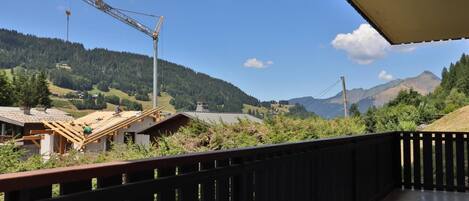 A construction site with a crane and a partially built structure, surrounded by a forested landscape and mountains in the background.
