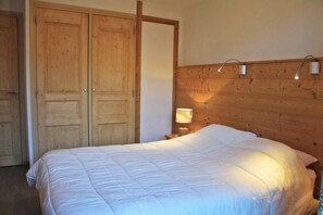 Quarto com cabeceira de madeira, cama com roupa de cama branca e mesa de cabeceira com abajur.