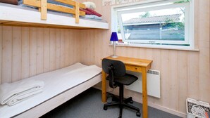 Une chambre avec un lit superposé, un bureau et une chaise, une fenêtre donnant sur un immeuble et un radiateur.