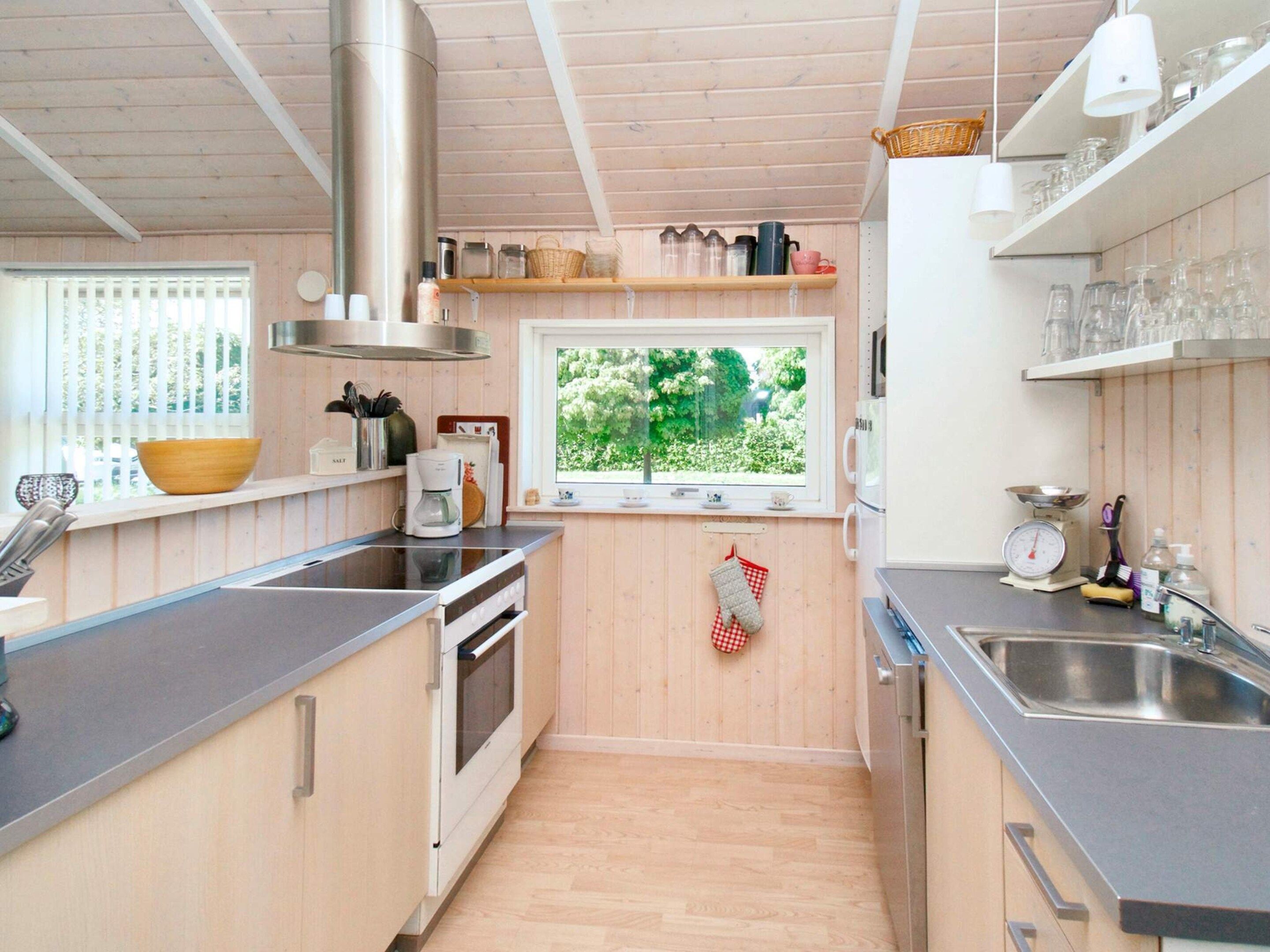 A compact kitchen with wooden cabinets, a stainless steel sink, and a window with a view of greenery.