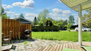Una terraza de madera con una parrilla, un porche cubierto y un patio trasero cercado.