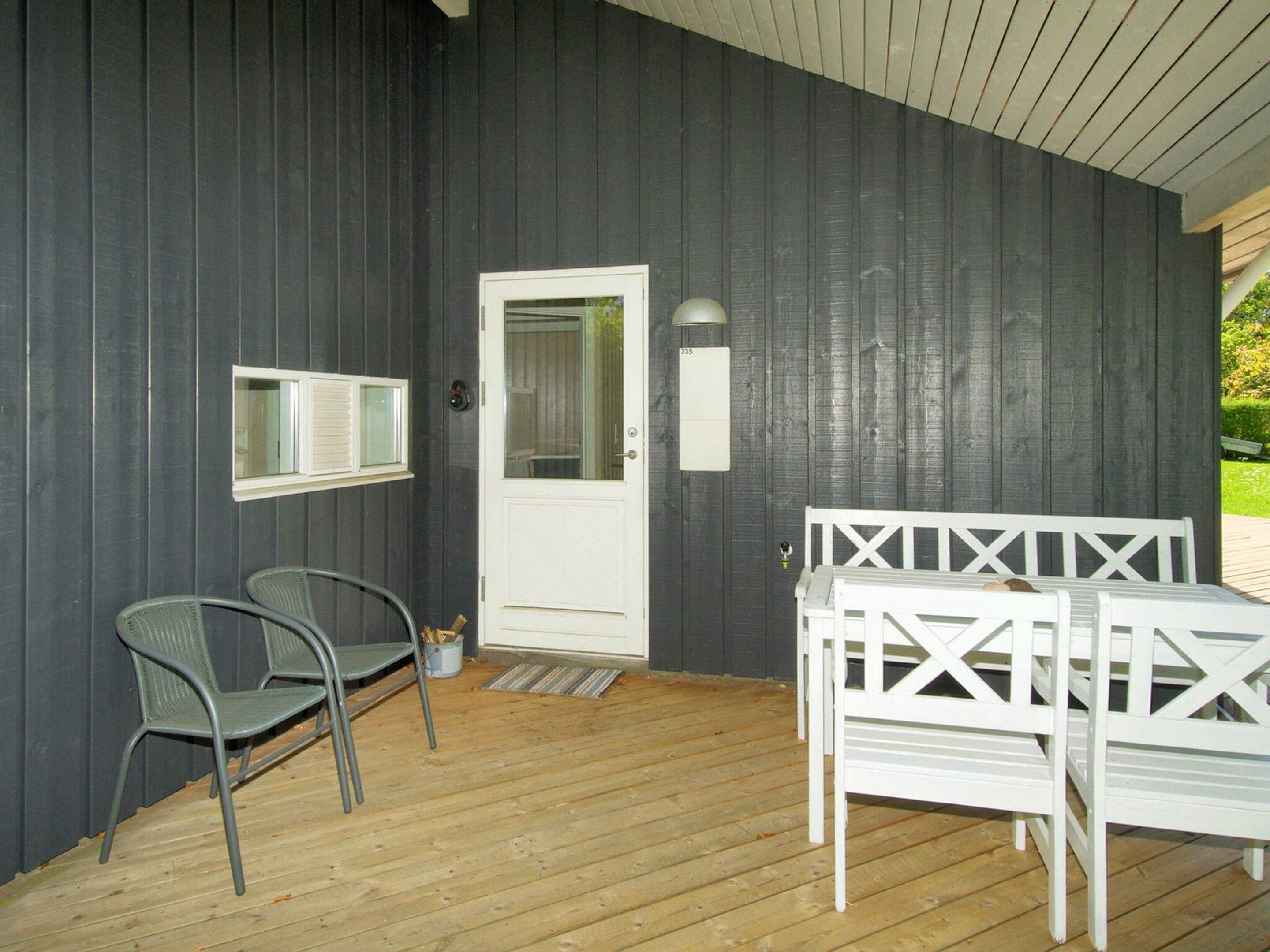 A covered outdoor area with a wooden deck, a white door, two metal chairs, and a white bench.