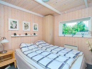 A bedroom with a bed, a bedside table, a lamp, and a window with a view of greenery. - 6 Person Holiday Home in Skibby (Skibby)