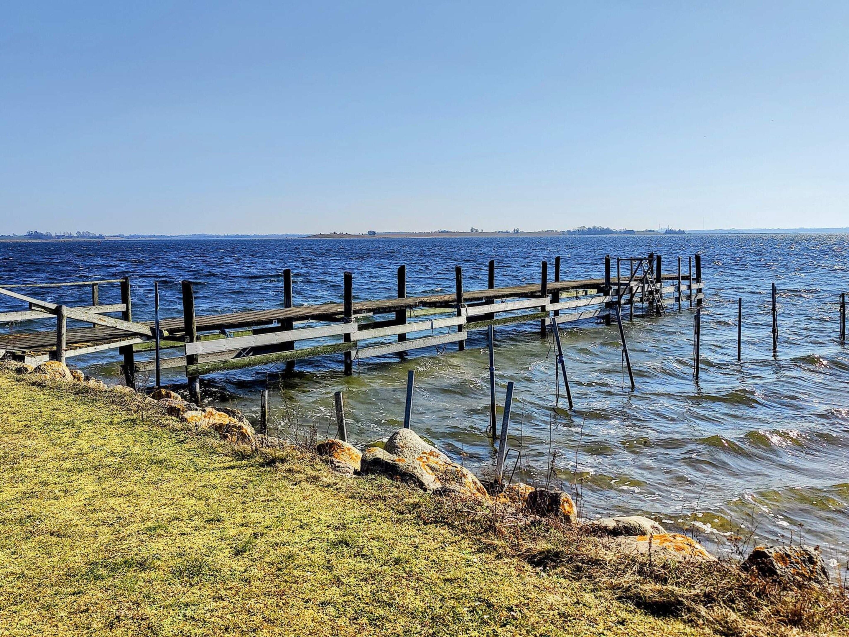 A wooden pier extending into calm water, surrounded by rocks and sparse vegetation.
