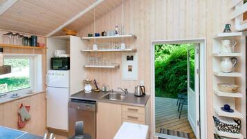 A compact kitchen with a refrigerator, microwave, and sink. There are shelves above the counter holding various kitchenware.