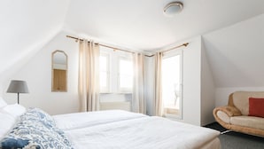 Ein Hotelzimmer mit einem großen Bett, einem Sessel, einer Lampe und einem Fenster mit Vorhängen.