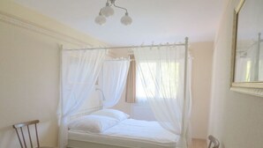 Een slaapkamer met een hemelbed, een stoel, een nachtkastje en een spiegel aan de muur.