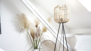 A modern, minimalist room with a sloped ceiling, a white sofa, a wicker floor lamp, and two white ceramic vases with plants. - Holiday Apartment Relaxing at the Monastery (Geisenheim)