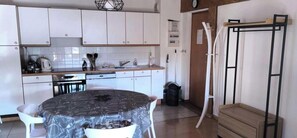 A compact kitchen with white cabinets, a round dining table, and a black trash bin.