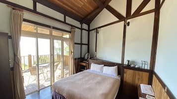 A bedroom with a large bed, wooden ceiling beams, a nightstand, a mirror, and a view of the outdoors.