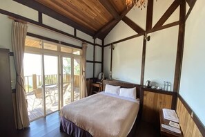 Un dormitorio con una cama grande, vigas de madera en el techo, una mesita de noche, un espejo y vistas al exterior.