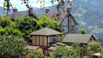 Un ensemble de maisons traditionnelles en bois, dotées de toits à deux versants, entourées d’une végétation luxuriante et avec des montagnes en arrière-plan.