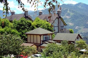A cluster of traditional wooden houses with pitched roofs, surrounded by lush greenery and mountains in the background.