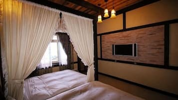 A room with a bed, curtains, a mounted television, and wooden beams.