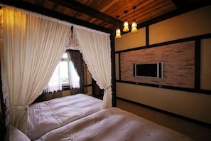 A room with a bed, curtains, a mounted television, and wooden beams.